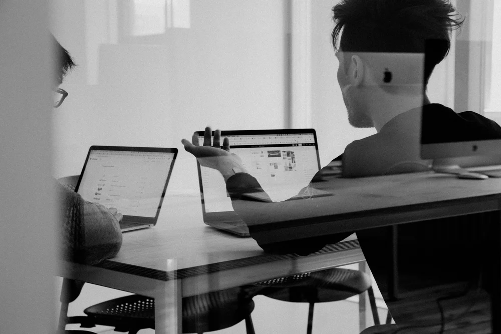 A support specialist working across two laptops in a meeting room